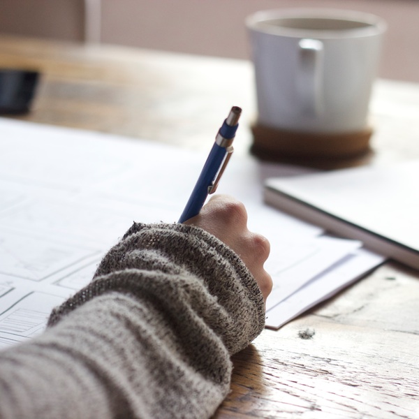 Person holding pencil with paper and mug.